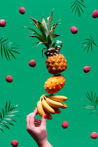Assortment of tropical fruits flying on green background. Pineapple, kiwano, kiwi , lichee and banana - levitation of exotic fruits.