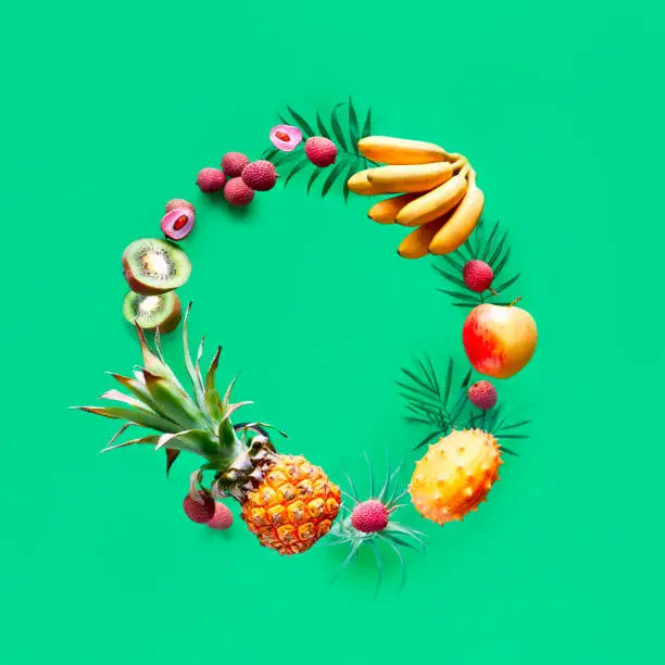 Assortment of tropical fruits flying in circle on green background. Square composition, copy-space. Pineapple, kiwano, kiwi , lichee and banana - levitation of exotic fruits.