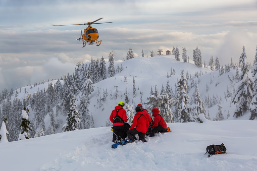 North Vancouver, British Columbia, Canada. North Shore Search and Rescue are rescuing a man skier in the backcountry of Seymour Mountain with a helicopter in winter during sunset.