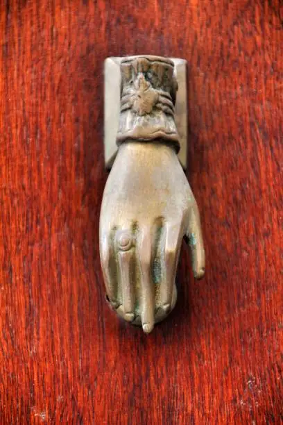 Golden doorknocker with hand shape on old brown wooden door in Porto, Portugal