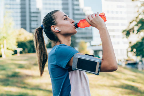 Sporty woman drinking water after exercise Sporty woman drinking water from bottle after exercising outdoors. Beautiful young woman sipping water from pink bottle after workout at park. energy drink stock pictures, royalty-free photos & images