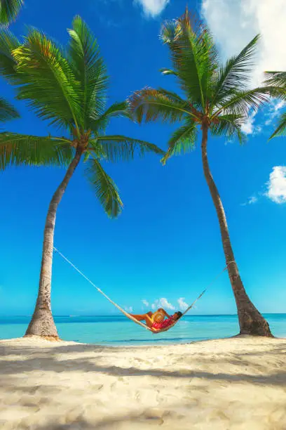 Photo of Young girl resting in a hammock under tall palm trees, tropical beach