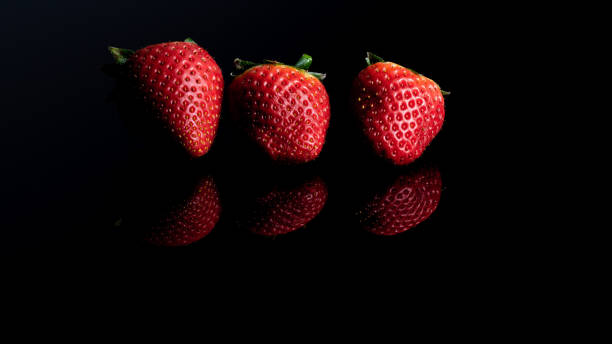 istock Three red strawberries in a row on a black background 1209968719