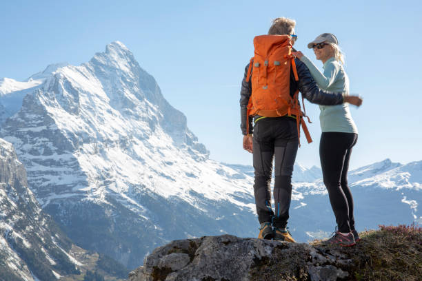 Hiking couple ascend alpine slope, in mountains They look over to distant view Grindlewald stock pictures, royalty-free photos & images