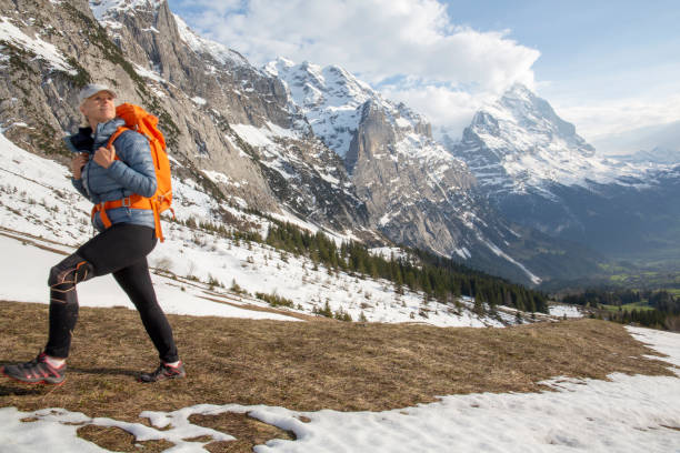 Female hiker ascends meadow slope, in mountains
