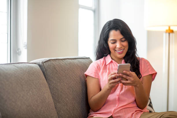 mujer hispana en casa leyendo su texto. - marcar usar el teléfono fotografías e imágenes de stock