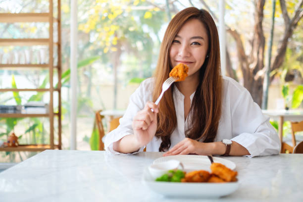 istock a beautiful asian woman eating fried chicken by fork in restaurant 1209999372