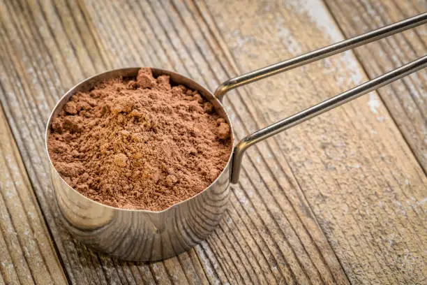 cacao powder in a metal measuring scoop against grunge wood background