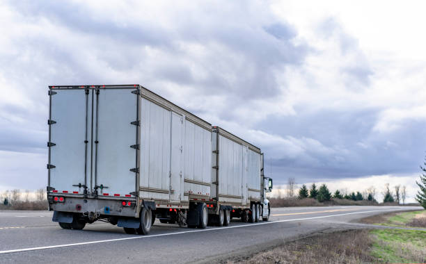 istock Big rig powerful semi truck transporting goods in two long semi trailers running on the straight road 1210006356