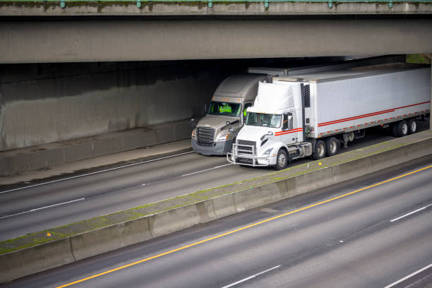 istock Two different industrial diesel big rig semi trucks with semi trailers transporting cargo running on the highway under the concrete bridge 1210007231