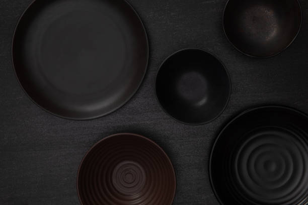 istock Group of empty blank black ceramic round bowls and plates on black stone blackground, Top view of traditional handcrafted kitchenware concept 1210010163