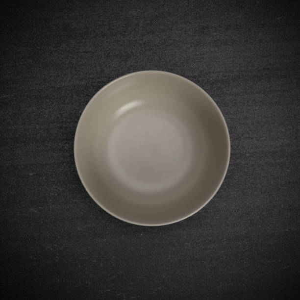 Empty blank white ceramic round bowl on black stone blackground with copy space, Top view of traditional handcrafted kitchenware concept