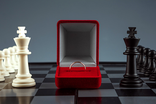 Chess pieces on a chessboard and a box with a golden ring, game. The concept of confrontation, career, competition, startup, truce, marriage, partnership