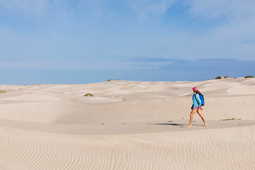 A woman is walking in sand dunes on Isla Magdalena with a blue sky overhead