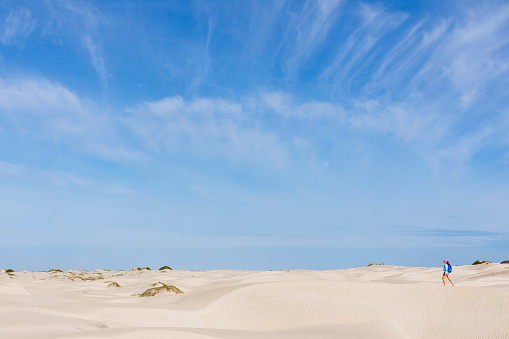 A woman is walking in sand dunes on Isla Magdalena with a blue sky overhead