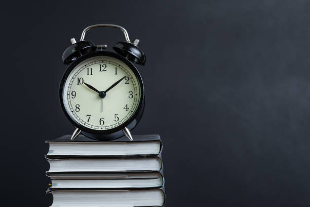 istock Alarm clock on stack of textbook with chalkboard or blackboard background copy space, time for reading, concentration in study, homework or educational concept 1210023583