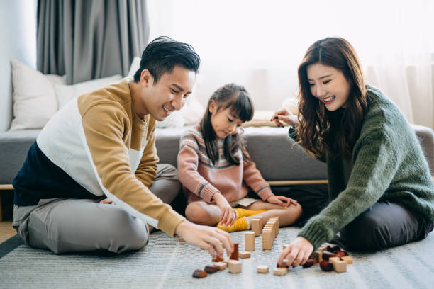 gioiosi genitori asiatici seduti sul pavimento nel soggiorno che si divertono e giocano a blocchi di legno con la figlia insieme - block togetherness happiness indoors foto e immagini stock