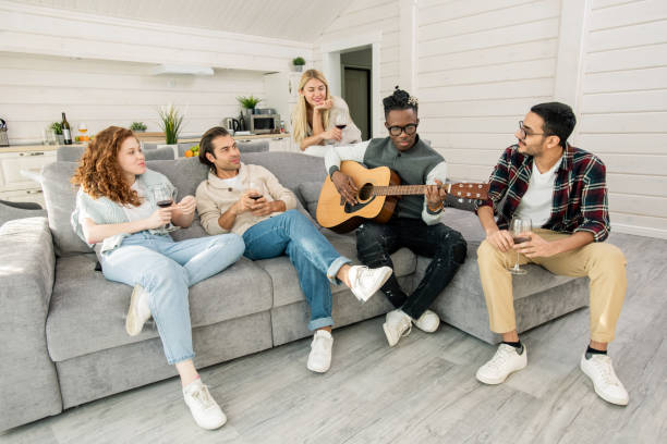 istock Young Africam man playing guitar while sitting on sofa among his friends 1210030480