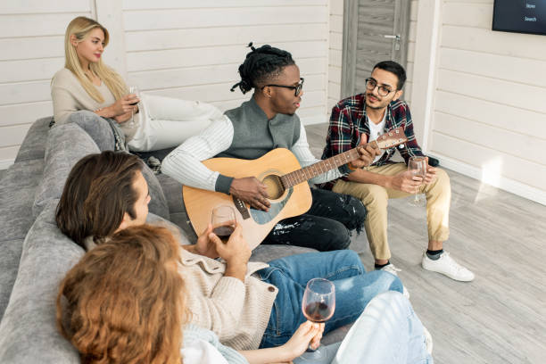 istock Young man with guitar singing for his friends sitting around him on couch 1210030486