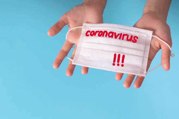 istock Hands on a blue background with a protective mask with the text Coronavirus.Concept coronavirus COVID quarantine. 1210037355