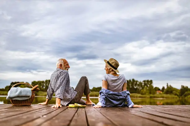 Photo of Happy senior couple talking during a picnic day on a pier at river.