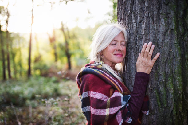 Senior woman on a walk in an autumn forest, hugging tree.