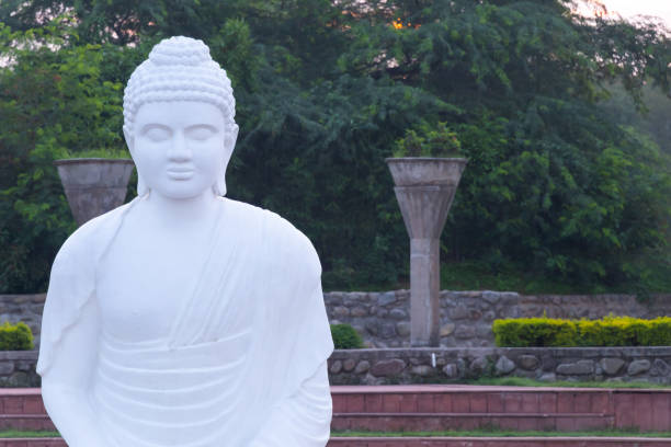 istock Front shot of a Buddha statue with green trees and concrete structures in the background 1210051320