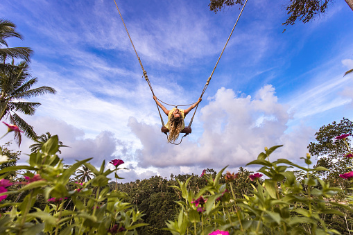 Young happy woman enjoying while swinging above the rainforest. Copy space.