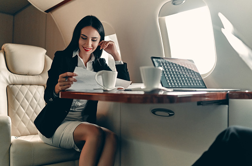 Successful young business woman working while flying in private jet.