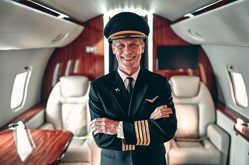 Experienced pilot in uniform standing in cabin of private jet. Pilot in command inside the aircraft.