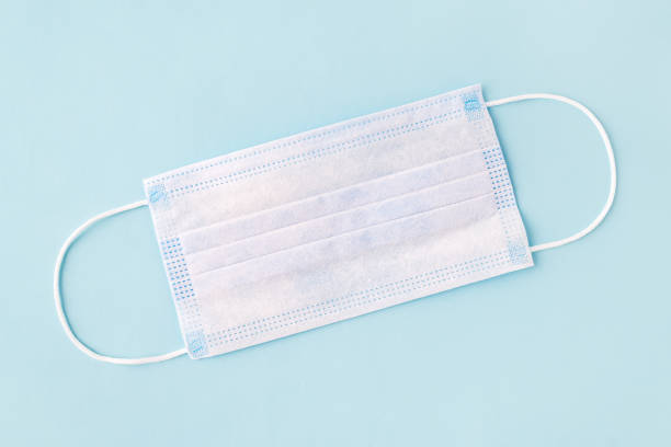 istock Disposable surgical mask on a blue background. Three-layer medical mask protects  from bacteria, viruses and dust, reduces the risk of infection. Airborne disease protection. 1210054207