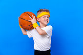Sporty little boy with basketball ball over blue studio background. Gym workout. Child sportsman. Activity. Sport. Fitness, health and energy. Success
