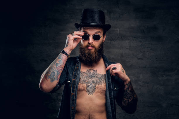 Portrait of brutal bearded man in sunglasses Portrait of brutal man with open denim shirt and tattooed chest. chest tattoos for men designs stock pictures, royalty-free photos & images