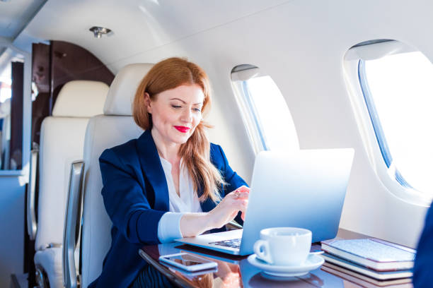 Businesswoman traveling by corporate jet Business travel. Elegant mature businesswoman sitting in private airplane and using a laptop. upper class photos stock pictures, royalty-free photos & images