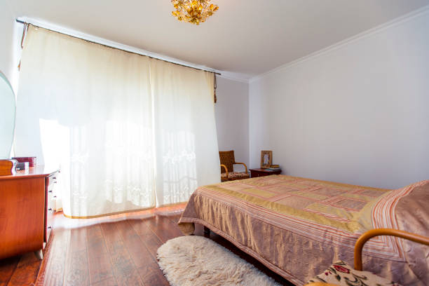 istock A large bedroom with a mahogany bed, wicker chairs, and an elegant dressing table with a semi-circular mirror. The bed has a beige blanket in squares. mahogany parquet 1210067156