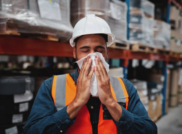 istock Young african manager coughing and feeling sick while covering mouth with handkerchief in warehouse 1210067411