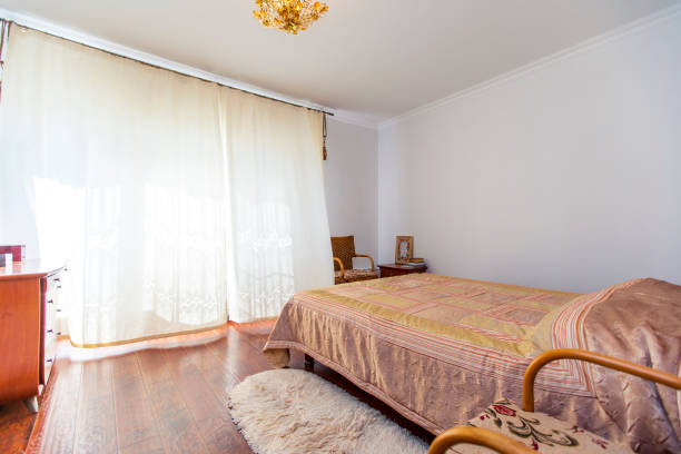 istock A large bedroom with a mahogany bed, wicker chairs, and an elegant dressing table with a semi-circular mirror. The bed has a beige blanket in squares. mahogany parquet 1210067713