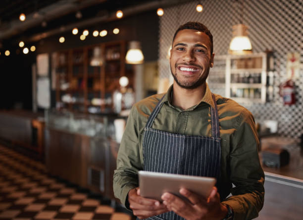 istock Young african-american man wearing apron standing using digital tablet in coffee shop 1210068794
