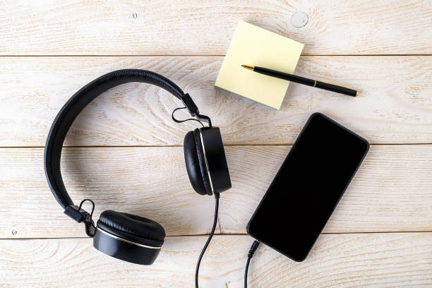 istock Smartphone, black headphones and pen with post-it notes block on a white wooden table. Modern personal device with touchscreen for music and communication. 1210077137