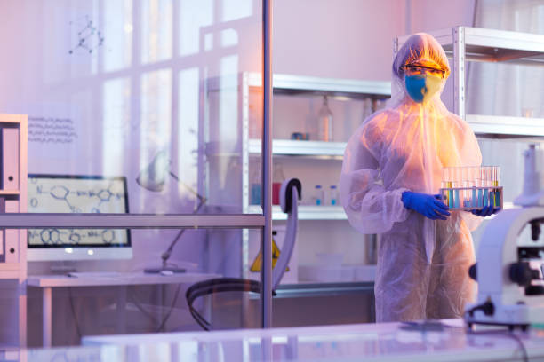 Unrecognizable Chemist With Test-Tubes Unrecognizable female chemist wearing disposable protective uniform holding test-tubes with liquids looking at camera, horizontal medium long shot, copy space cleanroom photos stock pictures, royalty-free photos & images