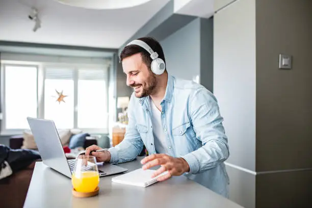 Young man is at home, with headphones and he is studying with laptop