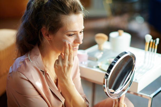 istock happy elegant woman applying cream and looking in mirror 1210089221