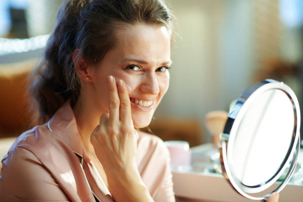 istock smiling housewife applying cream and looking in mirror 1210089303