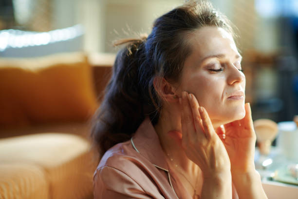 donna in casa moderna in soleggiata giornata invernale applicando crema - self massage foto e immagini stock