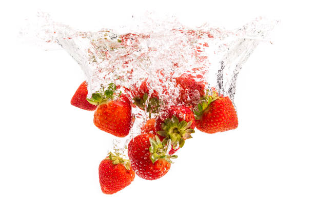 Strawberries drop into a glass of water, producing splashes and bubbles while showcasing freshness and vibrancy on a warm summer day. The scene captures a moment of enjoyment and relaxation.