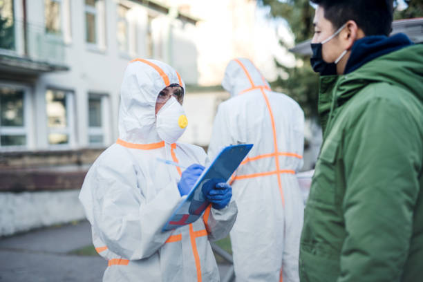 istock People with protective suits helping man outdoors, coronavirus concept. 1210091731