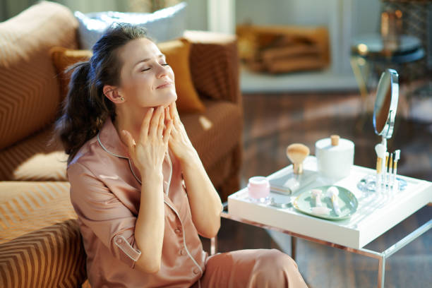 woman applying neck cream at modern home in sunny winter day - massage creme imagens e fotografias de stock