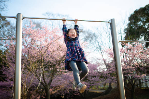 Girl playing a horizontal bar in a park where cherry blossoms bloom Girl playing a horizontal bar in a park where cherry blossoms bloom horizontal bar stock pictures, royalty-free photos & images