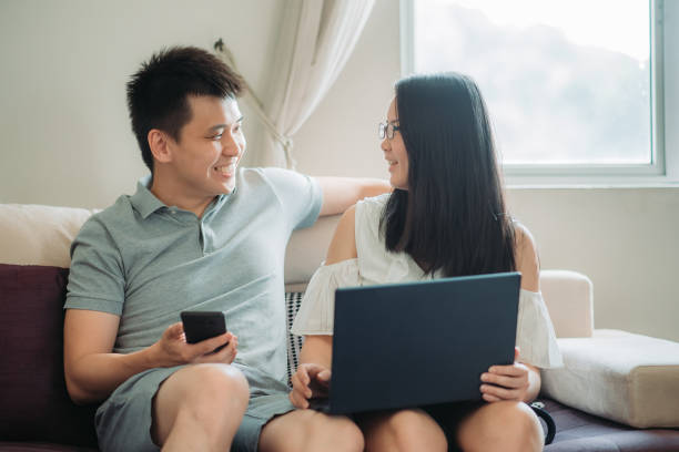 istock Asian chinese young couple bonding on the sofa, chatting while busy working on their laptop, mobile phone at living room 1210106278
