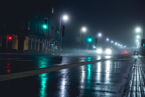 Light beams across the wet road as a lonely car makes it's way through storm soaked city